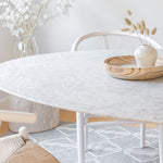 Load image into Gallery viewer, Flute Oval Marble Top Dining Table-Full Size by Style In Form. Lifestyle shot showing close-up of table top in a room, white wood dining chairs can also be seen in the background around. Shop vintage &amp; new home décor, lighting &amp; home furnishings as well as novelty gifts &amp; pet accessories online at blueigloo.ca
