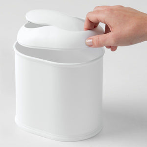 Vanity Waste Can by Inter Design. Front angled view of waste can with female hand lifting the lid slightly off the base of the can with her index finger, middle finger and thumb holding the lid on an off white background. Shop vintage & new home décor, lighting & home furnishings as well as novelty gifts & pet accessories online at blueigloo.ca
