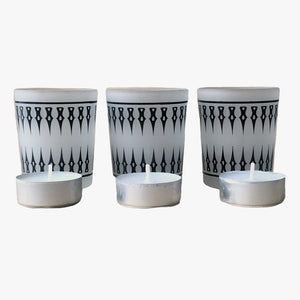 Damask Frosted Tea Light Holder-Set 3. A set of three frosted glass tea light holders with a black damask pattern. Shown in a straight line left to right with an inch between each holder with a single tea light in front of each holder on a white background. Shop tea light holders, decor, and decorative objects online at blueigloo.ca.