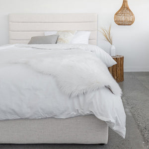 Justin Storage Bed-Tall, Cream by Style In Form. Lifestyle shot of bed in white room with concrete floor, bed dressed with duvet, pillows and fur throw. View from end of bed. Shop vintage & new home décor, lighting & home furnishings as well as novelty gifts & pet accessories online at blueigloo.ca