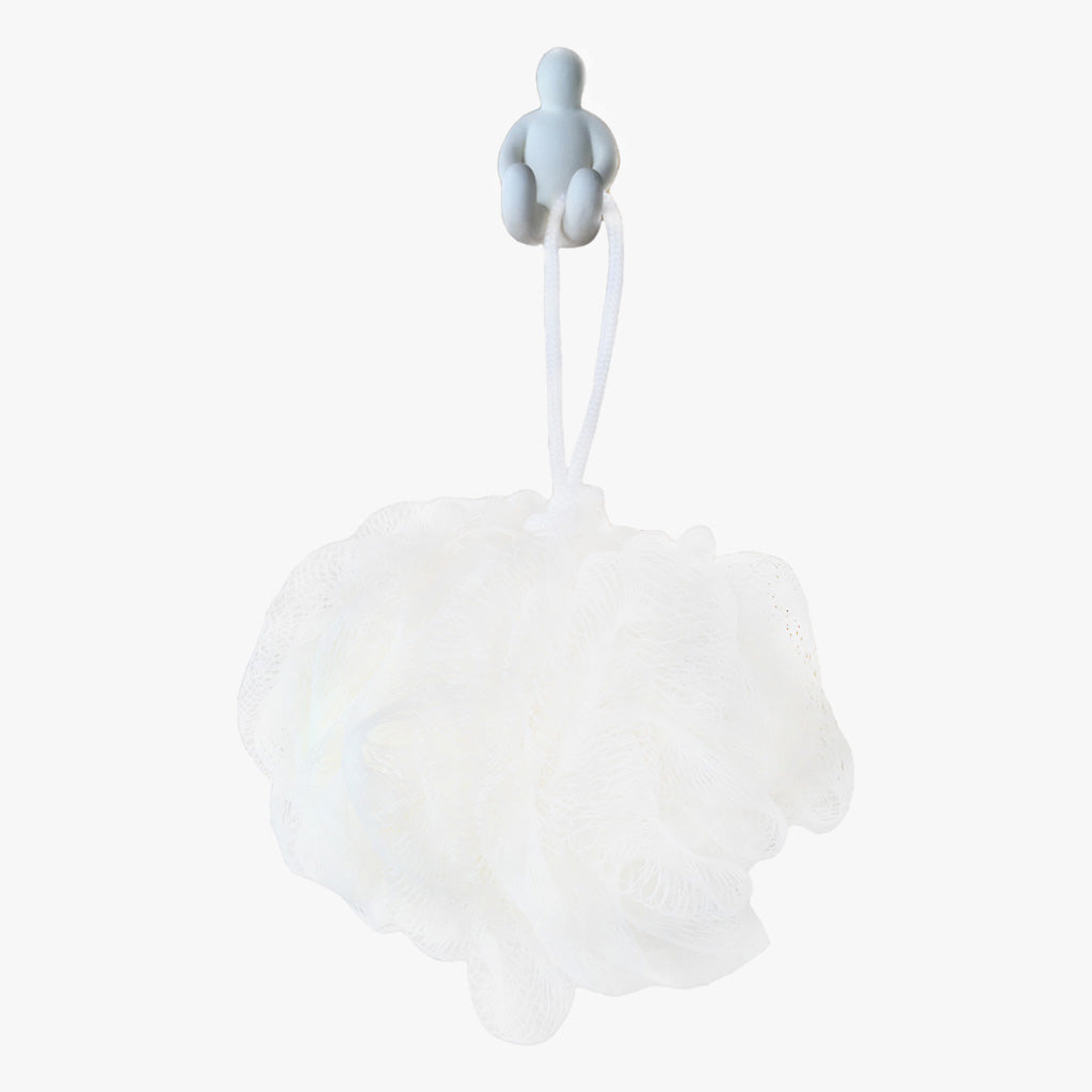 Resin Figure Hook, White. Front view showing hook with a white exfoliating loofah sponge hanging on it. A suction hook shaped like a person sitting with their arms resting on the top of their thighs. Legs are extended straight out in front of them. Shop suction hooks and other bath accessories at blueigloo.ca